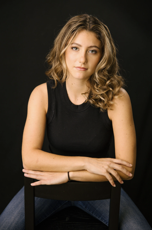 Tulia Henderson, theatrical headshot: seated with a level, direct gaze, against a dark background.